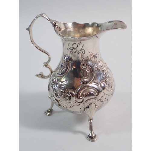 279 - A George III silver cream jug with later embossed flower and scrollwork decoration on three hoof fee... 