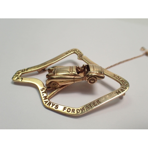 477 - An unusual 9 ct gold motor racing Stirling Moss brooch with racing car mounted on Goodwood race trac... 