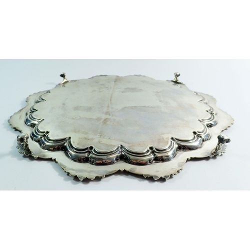 259 - A silver circular lobed tray with scrollwork border and engraved decoration, on four claw and ball f... 