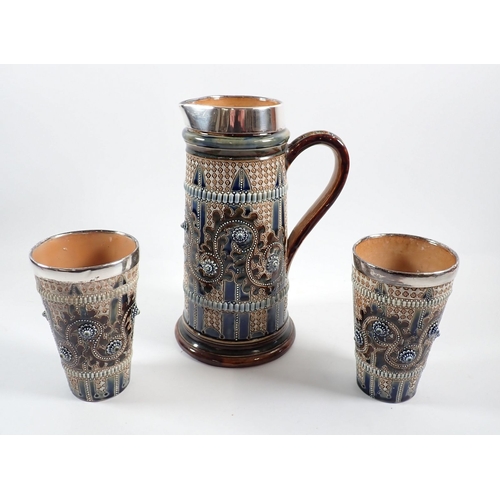 17 - A Doulton Lambeth stoneware tall jug, 25cm tall and two tumblers with applied decoration and silver ... 