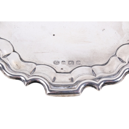 18 - A George V silver salver. Having a shaped and embossed border, a monogram engraved to the centre, on... 