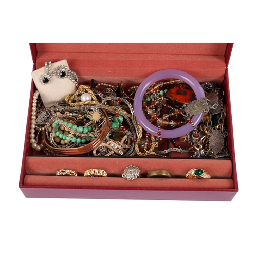 261 - A red jewellery box of mixed costume jewellery. Including rings, a lilac hardstone bangle, necklaces... 