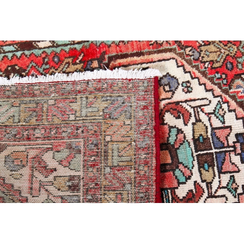 454 - A vintage Persian rug. The central cream diamond motif with floral details, mounted on a red ground,... 