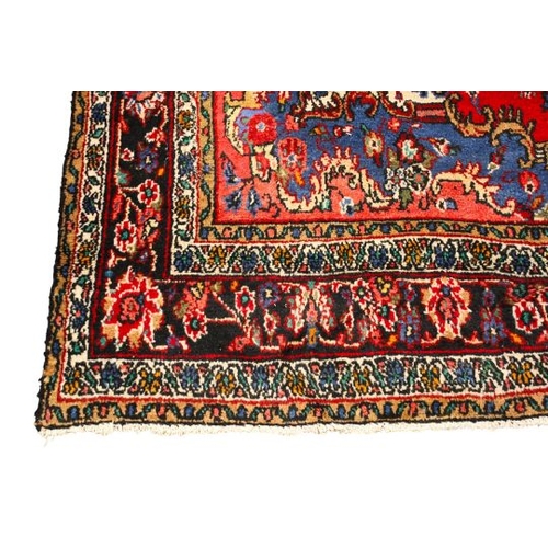 468 - A vintage Persian woollen rug. The central blue medallion on a red oval ground, surrounded by blue, ... 