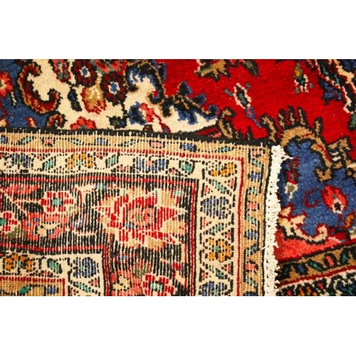 468 - A vintage Persian woollen rug. The central blue medallion on a red oval ground, surrounded by blue, ... 
