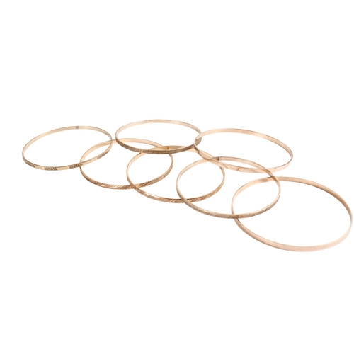 198 - Seven 9ct gold (tested) narrow flat bangles of various designs, some marked. Gross weight 49.8g.