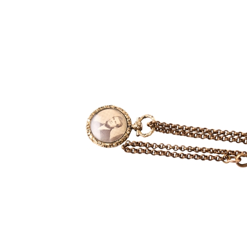 254 - A yellow metal photograph pendant on a gold plated chain. The pendant with scroll border and pattern... 