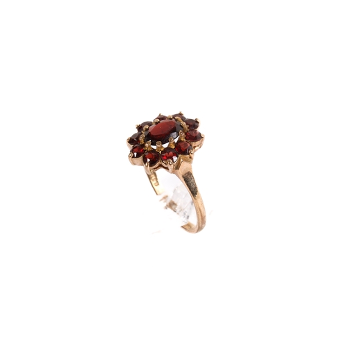 129 - A 9ct gold garnet cluster ring. Set with ten small stones around the central oval faceted stone, siz... 