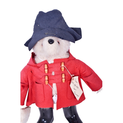 228 - A vintage plush model of Paddington Bear. Having brown hair, a red felt coat, black hat and wellingt... 
