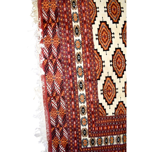 521 - A large Turkamen style wool rug on a red ground. Having multiple geometric borders with a Gul motif ... 