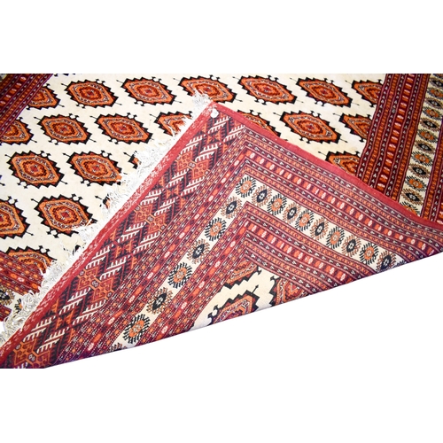 521 - A large Turkamen style wool rug on a red ground. Having multiple geometric borders with a Gul motif ... 