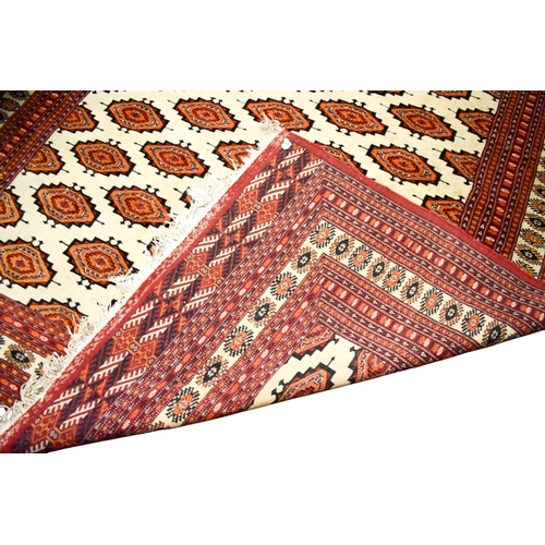 521 - A large Turkamen style wool rug on a red ground. Having multiple geometric borders with a Gul motif ... 
