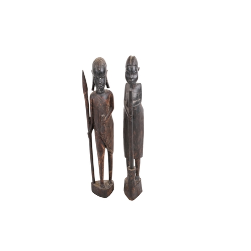 334 - A pair of carved African figures. Modelled as a man holding a weapon and a woman holding a broom, he... 