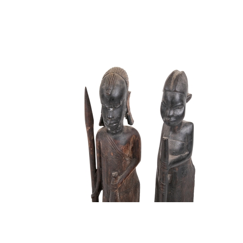 334 - A pair of carved African figures. Modelled as a man holding a weapon and a woman holding a broom, he... 