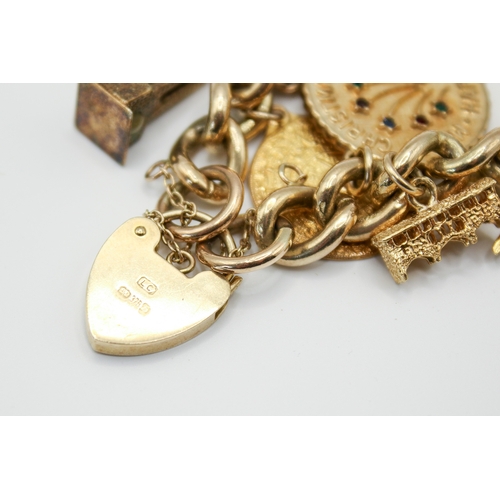 147 - A 9ct gold charm bracelet with 23 assorted gold and yellow metal charms. Charms include a post box, ... 