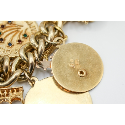 147 - A 9ct gold charm bracelet with 23 assorted gold and yellow metal charms. Charms include a post box, ... 