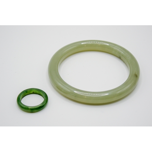 181 - A pale green jade bangle and a ring. The bangle with pale cloudy sections and a couple of darker spo... 