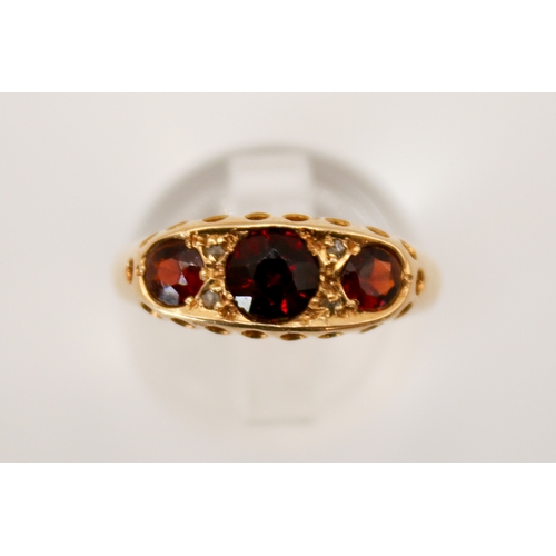 69 - An 18ct gold and garnet three stone ring. In a pierced setting, the central stone circa 4.5mm diamet... 