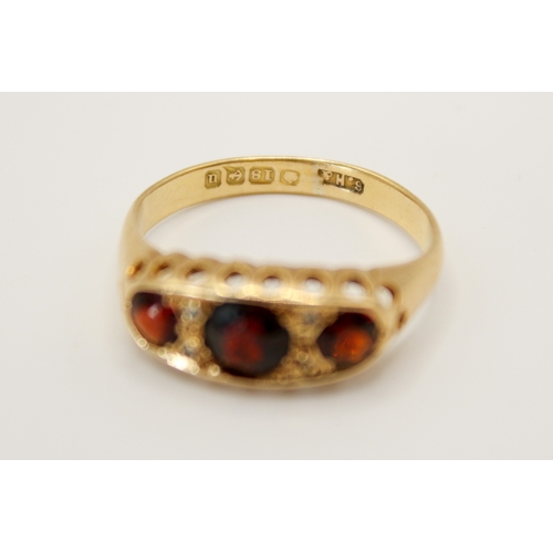 69 - An 18ct gold and garnet three stone ring. In a pierced setting, the central stone circa 4.5mm diamet... 
