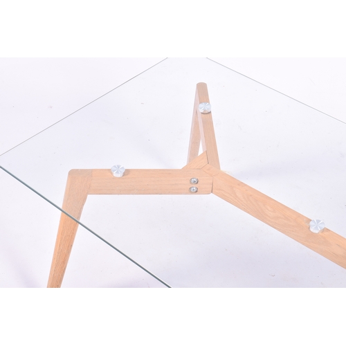 22 - A modern glass top coffee table on light oak angled supports. Small chip to corner of glass. H45cm x... 