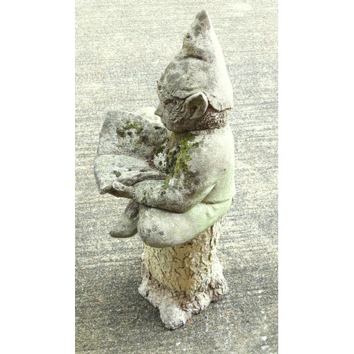 340 - Composition figure of a gnome, sitting crossed legged reading a book, on a composition tree trunk ba... 