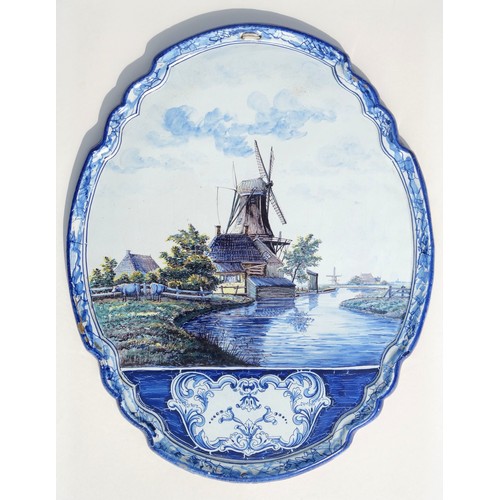 160 - Dutch Delft shaped oval plaque painted with a river, 2 cattle, 2 windmills, buildings, trees and flo... 