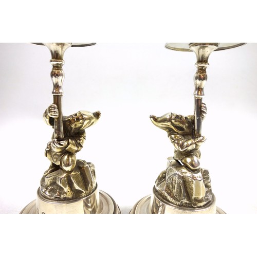 20 - Pair of novelty silver candlesticks, each modelled as a gnome or dwarf holding the urn shaped sconce... 
