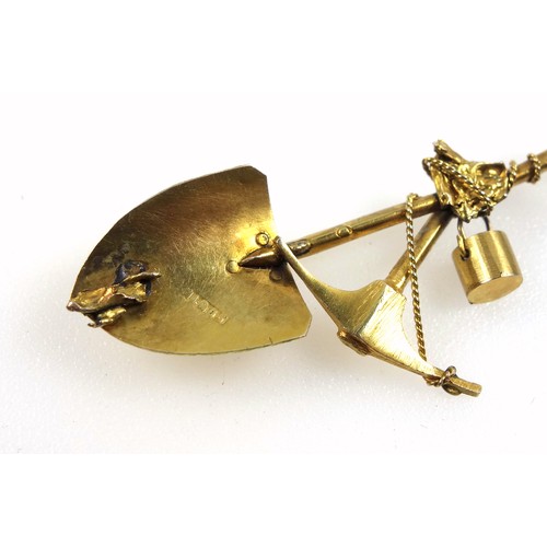 140 - A yellow metal 'gold prospectors' brooch, in the form of a crossed spade and pickaxe, suspending a b... 