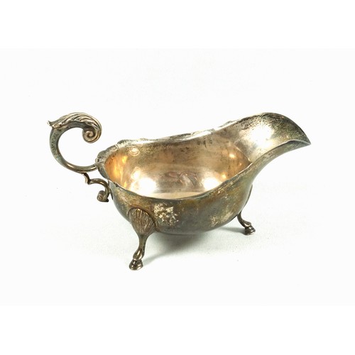 508 - George V silver sauceboat, of conventional form with a shaped rim and flying scroll handle, on 3 hoo... 