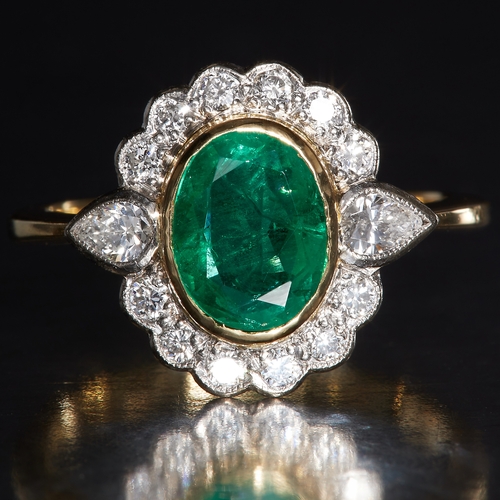 22 - EMERALD AND DIAMOND CLUSTER RING, in 18 ct. gold. Set with a central oval emerald of approx. 1.80 ct... 