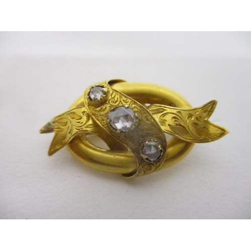 115 - A Victorian gold coloured metal and three stone diamond brooch, fashioned as ribbons on an oval back... 