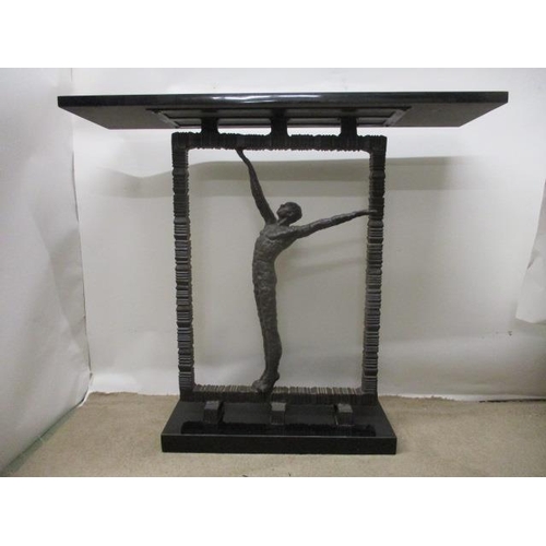 125 - A contemporary cast bronze hall table having a black marble top, over a man with outstretched arms, ... 