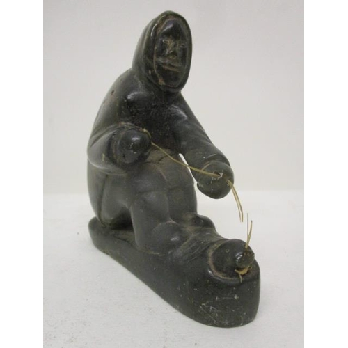 298 - A Canadian carved, green soapstone figure of an Inuit catching a fish through a hole in the ice, 3 1... 