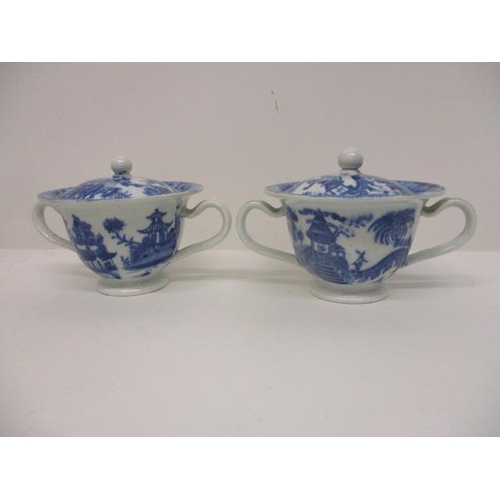 74 - A pair of Pearlware blue and white custard cups, with domed covers and twin handles, decorated with ... 