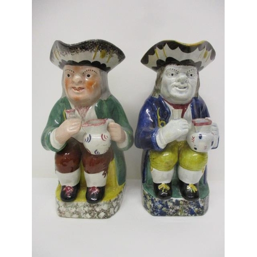 76 - An early 18th century and a 19th century Toby jug, each holding a jug and a glass on a plinth, 10