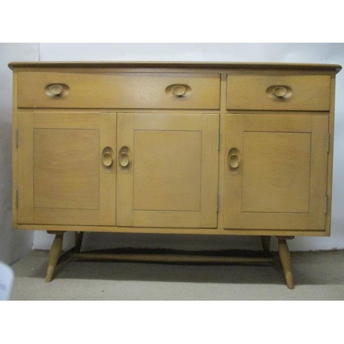 1 - A mid 20th century Ercol Windsor light elm sideboard with a long and a short drawer over three doors... 