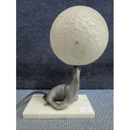 43 - An Art Deco style table lamp in the form of a seal, mounted on a white marble base, balancing a fros... 
