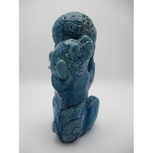 28 - A 20th century Chinese blue glazed Foo dog on its haunches, holding up a ball, 9 1/2