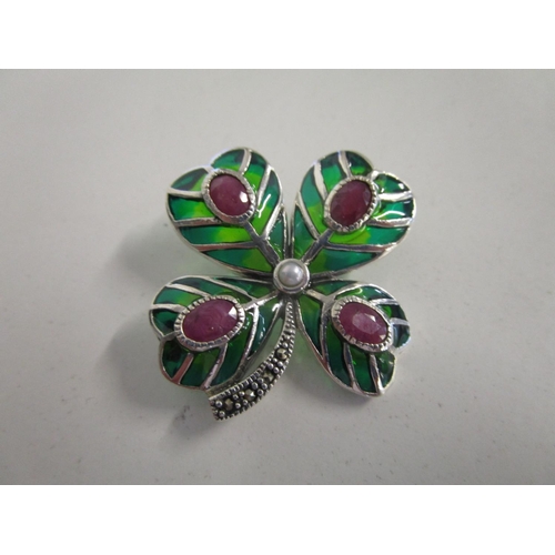 1 - A silver and enamelled brooch fashioned as a four leaf clover, set with rubies, a pearl and marcasit... 