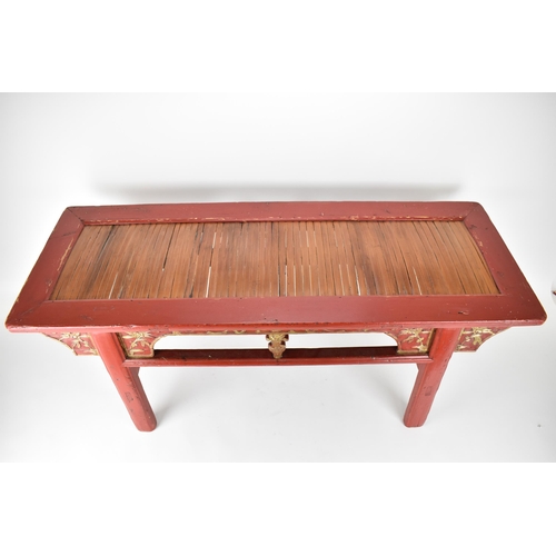 107A - A late 20th century Chinese red painted opium table with a bamboo, slatted top, over a carved and gi... 