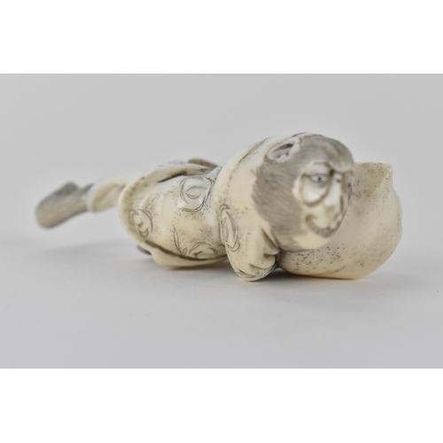 78 - A Japanese Meiji period early 20th century ivory netsuke of a monkey wearing a nappy and clutching a... 