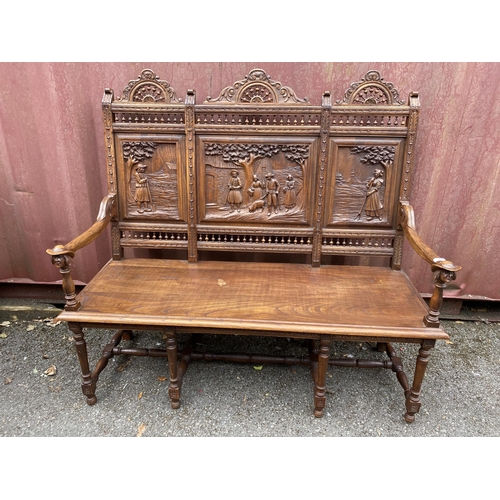 174 - An early 20th century French carved oak bench with a carved, pierced panelled back with country scen... 