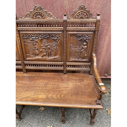 174 - An early 20th century French carved oak bench with a carved, pierced panelled back with country scen... 