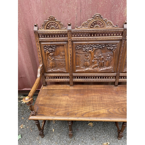 174 - An early 20th century French carved oak bench with a carved, pierced panelled back with country scen... 