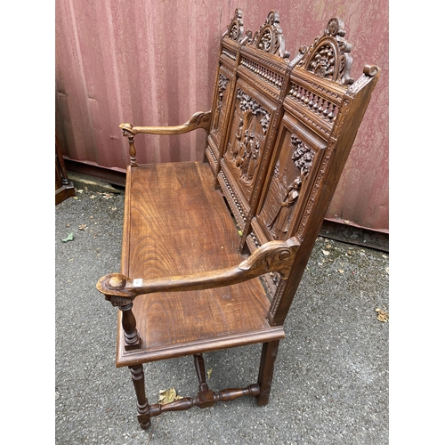 174 - An early 20th century French carved oak bench with a carved, pierced panelled back with country scen... 