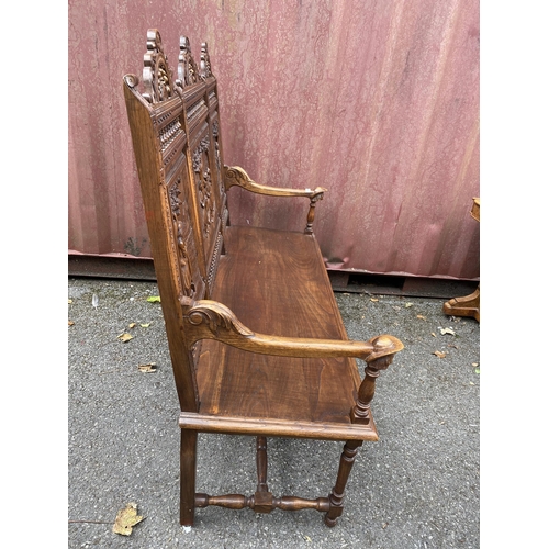 174 - An early 20th century French carved oak bench with a carved, pierced panelled back with country scen... 