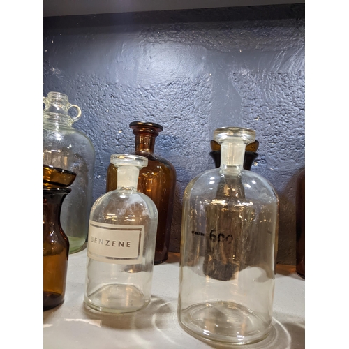 76 - Thirteen clear and brown glass chemist bottles to include one inscribed Benzene and another stamped ... 