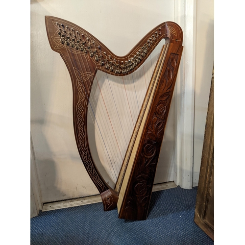 94 - A wooden knee harp with twenty seven strings and carved ornament in a soft carrying case, 89cm high
... 