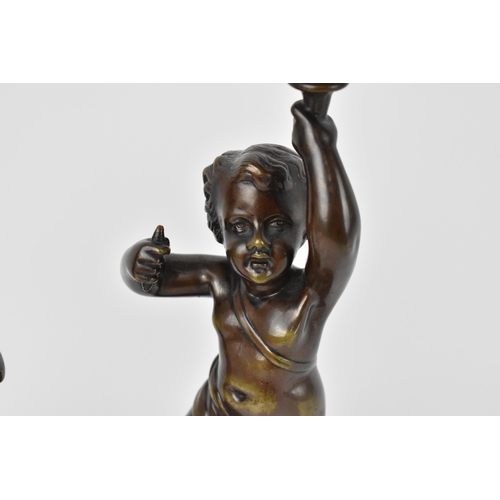 137 - A pair of late 19th century patinated bronze figural lamps, each modelled as a putto holding the lig... 