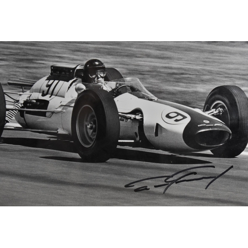 195 - A signed reprinted photograph of Dan Gurney in a racing car, within a glazed frame, 30 x 40 cm